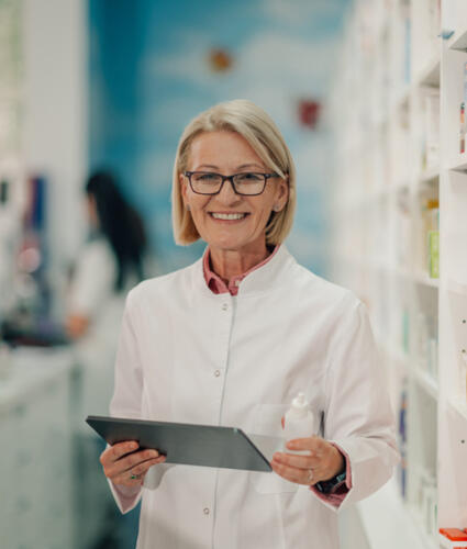 Senior female pharmacist holding nasal spray and using digital tablet in a pharmacy