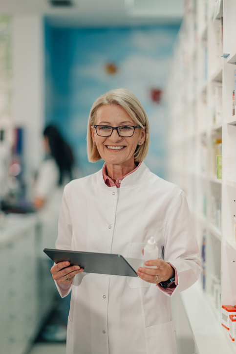 Senior female pharmacist holding nasal spray and using digital tablet in a pharmacy